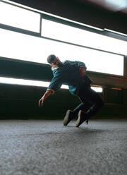 Full body of male in casual clothes jumping while dancing on asphalt road standing on tiptoes near contemporary wall with glowing lamps - ADSF42534