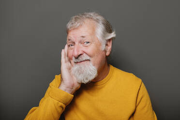 Porträt eines älteren grauhaarigen Mannes in gelbem Pullover vor grauem Hintergrund, der lächelt - ADSF42583
