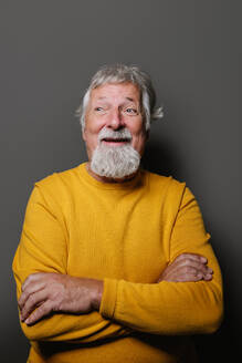 Porträt eines älteren grauhaarigen Mannes in gelbem Pullover, der vor einem grauen Hintergrund steht und lächelt - ADSF42585