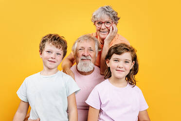 Fröhliche Großmutter mit Brille, die ihren Großvater umarmt, mit Enkelkindern in Freizeitkleidung, die in die Kamera schauen und gemeinsam Spaß haben - ADSF42588
