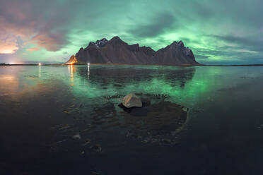 Atemberaubendes Polarlicht, das nachts bei kaltem Wetter in Island über eine raue Steinformation in der Nähe des eisigen Ozeans scheint - ADSF42613