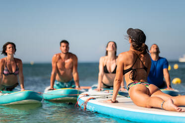 Side view of female instructor in front of couple on paddleboards doing Urdhva Mukha Svanasana in sea water on sunny day - ADSF42664