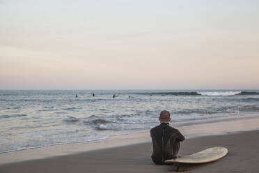 Mann mit Surfbrett am Strand sitzend - FOLF11932