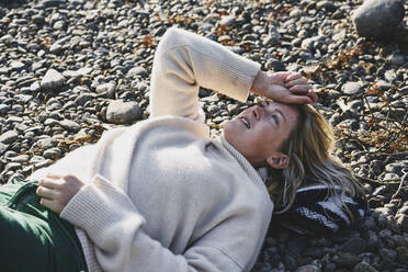 Woman in sweater lying on riverbank - FOLF11957