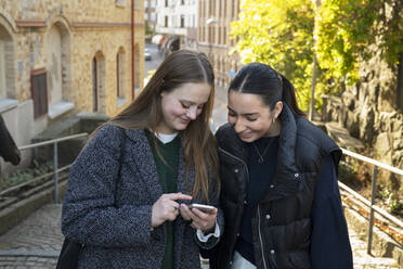 Young women using smart phone on city street - FOLF11979