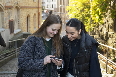 Junge Frauen benutzen ein Smartphone auf einer Straße in der Stadt - FOLF11979