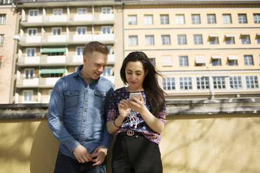 Woman showing man her smartphone on balcony - FOLF12023