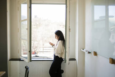 Young woman using smartphone by window - FOLF12090