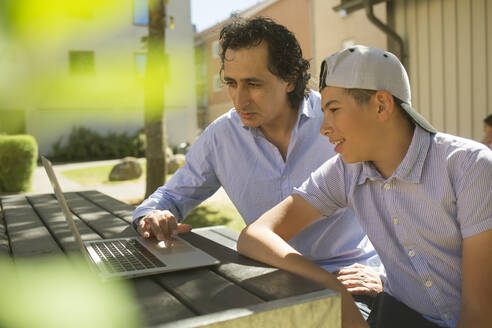 Man helping his son study at outdoor table - FOLF12108