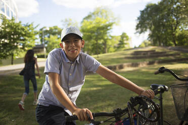 Smiling boy with bicycle in park - FOLF12110