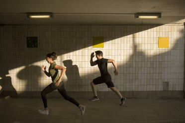 Young man and woman jogging by tiled wall - FOLF12122