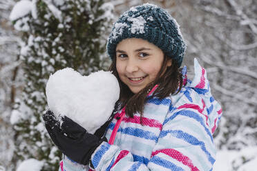 Lächelndes Mädchen in warmer Kleidung zeigt herzförmigen Schneeball - OSF01274