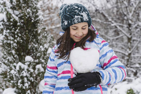 Lächelndes Mädchen hält herzförmigen Schneeball im Winter - OSF01275