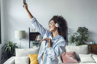 Woman gesturing and enjoying listening to music through headphones at home - JSRF02325