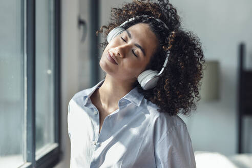 Frau mit geschlossenen Augen, die zu Hause über Kopfhörer Musik hört - JSRF02328