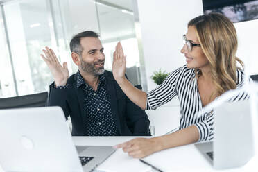 Business colleagues giving high five in office - JSRF02367