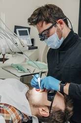 Zahnarzt, der die Zähne eines Patienten mit Geräten in der Klinik untersucht - VSNF00266