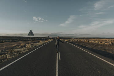 Woman walking in middle of road at sunrise - DMGF00910