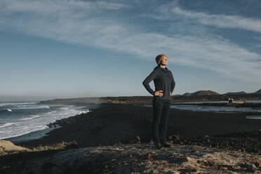 Frau stehend mit Händen auf der Hüfte am Strand von Janubio, Lanzarote, Kanarische Inseln, Spanien - DMGF00919