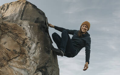 Glückliche Frau klettert auf einen Felsen vor dem Himmel - DMGF00934