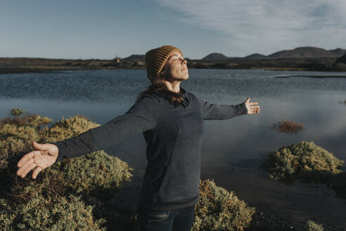 Woman with arms outstretched enjoying sunlight at lake - DMGF00936