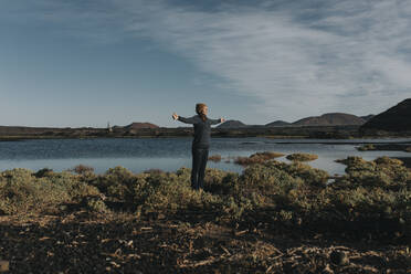 Woman standing with arms outstretched by lake - DMGF00938