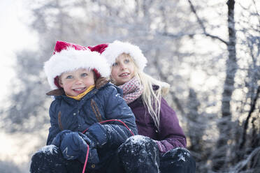 Happy brother and sister wearing Santa hats sitting on sled - NJAF00169