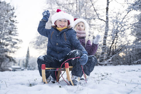 Fröhlicher Bruder und Schwester mit Weihnachtsmannmützen auf dem Schlitten sitzend - NJAF00170