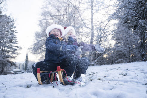 Fröhlicher Junge und Mädchen mit Weihnachtsmannmützen spielen im Schnee - NJAF00171