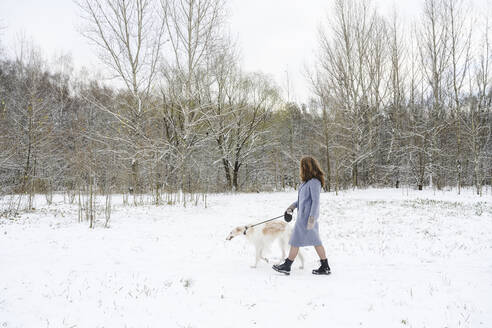 Ältere Frau geht mit Windhund im Winterpark spazieren - EYAF02484