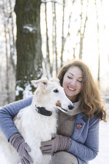 Happy mature woman with white greyhound dog in winter park - EYAF02488