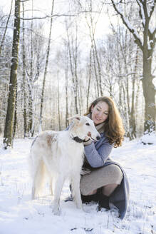 Happy mature woman stroking greyhound dog in winter park - EYAF02490