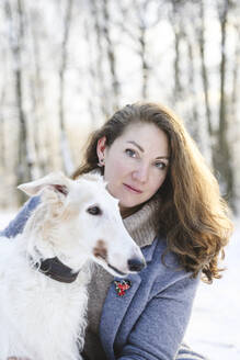Mature woman with white greyhound dog at winter park - EYAF02491