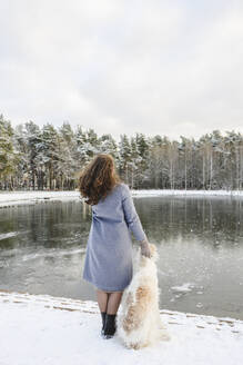 Mature woman standing with greyhound dog in front of frozen lake - EYAF02494