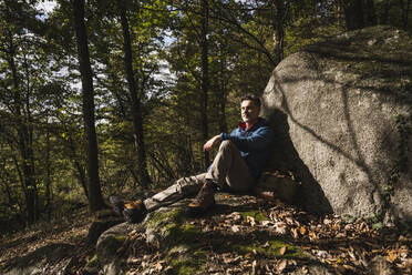 Älterer Mann mit geschlossenen Augen sitzt an einem Felsen im Wald - UUF27835
