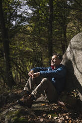 Nachdenklicher Mann sitzt an einem Felsen im Wald - UUF27838