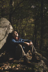 Älterer Mann mit geschlossenen Augen entspannt sich an einem Felsen im Wald - UUF27839