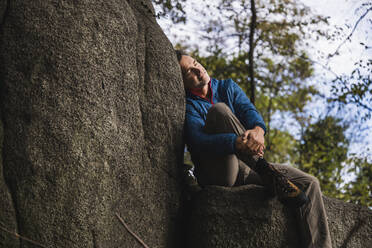 Mann mit geschlossenen Augen lehnt an einem Felsen vor einem Baum - UUF27844