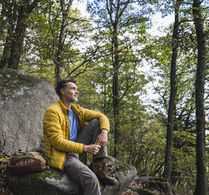 Mann mit Rucksack sitzt auf einem Felsen im Wald - UUF27853