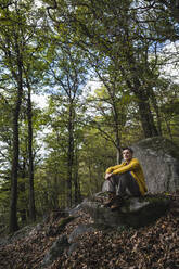 Man day dreaming on rock in front of tree at forest - UUF27856