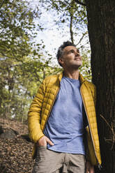 Thoughtful mature man with hand in pocket leaning on tree - UUF27860