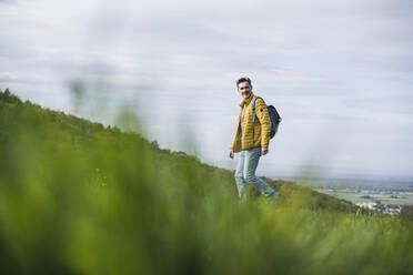 Lächelnder Mann mit Rucksack beim Wandern auf einem Berg - UUF27871