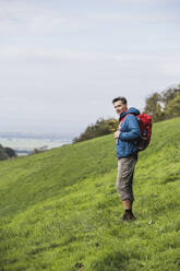 Älterer Mann beim Wandern mit Rucksack auf einer Wiese am Himmel - UUF27883