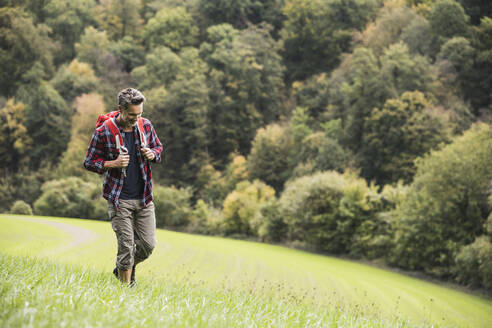 Älterer Mann mit Rucksack wandern auf Gras durch Wald im Urlaub - UUF27906