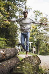 Mature man with arms outstretched walking on log - UUF27911