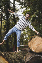 Glücklicher reifer Mann mit ausgestreckten Armen auf einem Baumstamm balancierend - UUF27912
