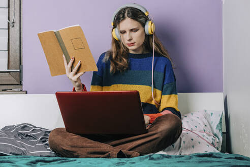 Mädchen mit Laptop bei den Hausaufgaben auf dem Bett sitzend vor der Wand - VSNF00284