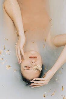 Girl taking bath with flowers in bathtub - VSNF00292