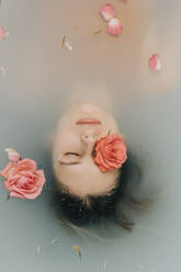 Girl with eyes closed taking bath with roses in bathtub - VSNF00294