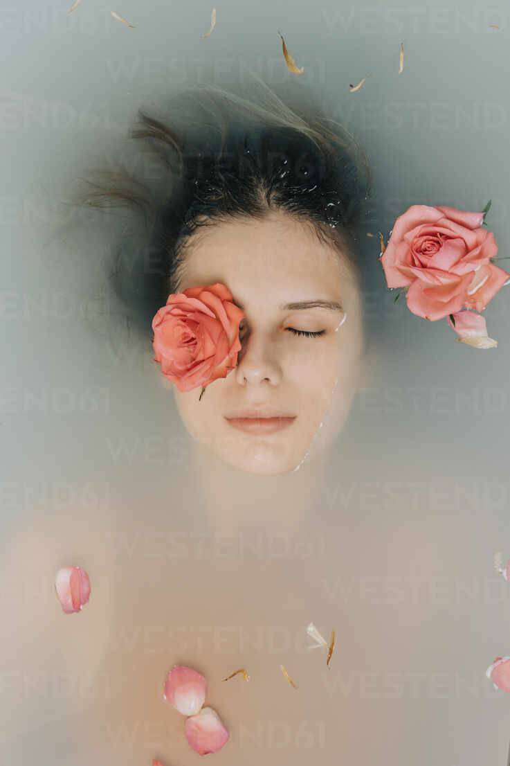 Girl with eyes closed taking bath with roses in bathtub stock photo